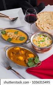 Indian Curry Food Spread On A Fancy Dinner Table With Rice, Laccha Paratha, Lamb Aam Wala, Saffron Malai Kofta, Red Wine.