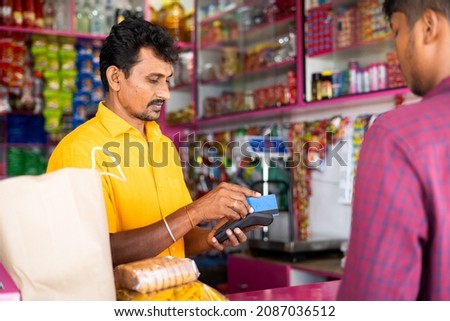 Indian customer making payment using credit card at groceries or Kirana shop - concept of digital or cashless payment, finance and Small business.