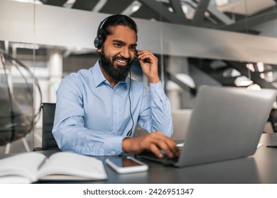 Indian Customer Support Manager Man In Headset Working With Laptop Computer In Office, Consulting Clients, Eastern Guy Sitting At Desk And Smiling, Free Space. Hotline Operator - Powered by Shutterstock