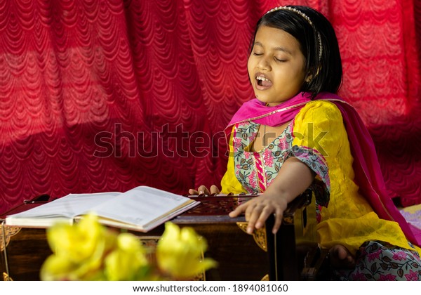 an Indian cute girl child singing and playing\
harmonium in ethnic dress