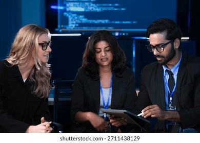 An Indian developer asks a question about AI code during a large IT department meeting. The engineering team is in a SOC, analyzing cybersecurity data on screens.