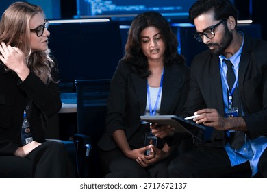 An Indian developer asks a question about AI code during a large IT department meeting. The engineering team is in a SOC, analyzing cybersecurity data on screens.