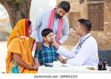 Indian Doctor examine little kid boy patient at village, woman wearing sari with her husband and son consulting medical person,Rural India healthcare concept.