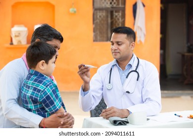 Indian Doctor examine little kid boy patient fever at village with digital thermometer, Father with his son consulting medical person,Rural India healthcare camp concept.