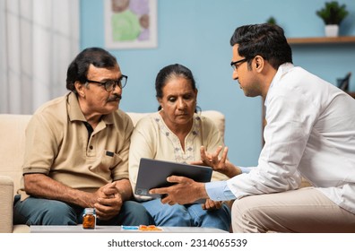 Indian doctor explaining from digital tablet to senior couple about medical report at home - concept of technology, health care support and home consultation. - Powered by Shutterstock