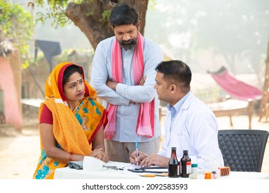 Indian Doctor explaining medical test or prescribing medicine to the patient at village, woman wearing sari with her husband getting examine by medical person,Rural India healthcare concept.