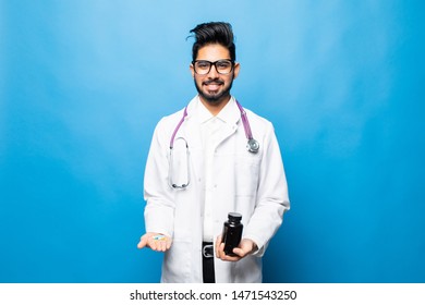 Indian Doctor In Uniform Pointing A Medicine Bottle And Looking At Camera While Standing Isolated On Blue Background