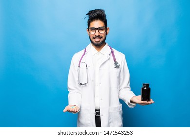 Indian Doctor In Uniform Pointing A Medicine Bottle And Looking At Camera While Standing Isolated On Blue Background