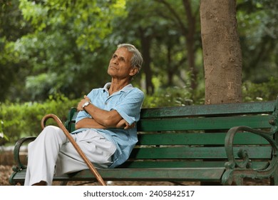 Indian elderly man sitting on a bench and thinking while sitting on bench with walking stick at park - Powered by Shutterstock