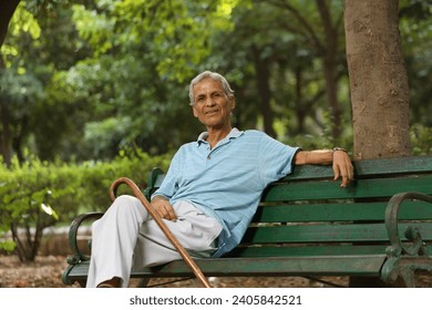 Indian elderly man sitting on a bench and thinking while sitting on bench with walking stick at park - Powered by Shutterstock