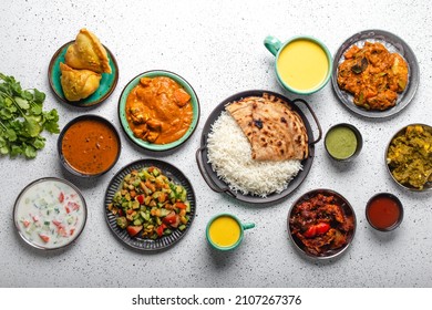 Indian Ethnic Food Buffet On White Concrete Table From Above: Curry, Samosa, Rice Biryani, Dal, Paneer, Chapatti, Naan, Chicken Tikka Masala, Mango Lassi, Dishes Of India For Dinner Background