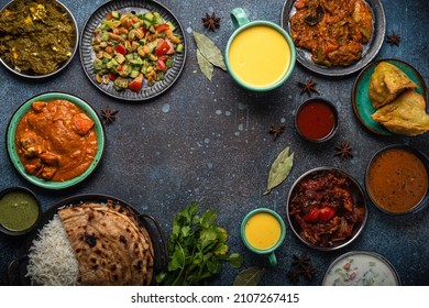 Indian Ethnic Food Buffet On Concrete Table From Above: Curry, Samosa, Rice Biryani, Dal, Paneer, Chapatti, Naan, Chicken Tikka Masala, Mango Lassi, Dishes Of India For Dinner Background Copy Space