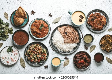 Indian Ethnic Food Buffet On White Concrete Table From Above: Curry, Samosa, Rice Biryani, Dal, Paneer, Chapatti, Naan, Chicken Tikka Masala, Mango Lassi, Dishes Of India For Dinner Background