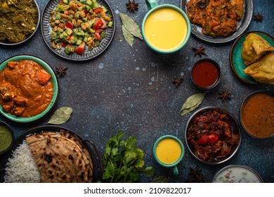 Indian Ethnic Food Buffet On Concrete Table From Above: Curry, Samosa, Rice Biryani, Dal, Paneer, Chapatti, Naan, Chicken Tikka Masala, Mango Lassi, Dishes Of India For Dinner Background Copy Space