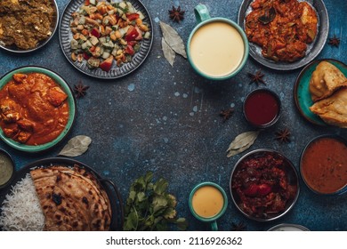 Indian Ethnic Food Buffet On Concrete Table From Above: Curry, Samosa, Rice Biryani, Dal, Paneer, Chapatti, Naan, Chicken Tikka Masala, Mango Lassi, Dishes Of India For Dinner Background Copy Space