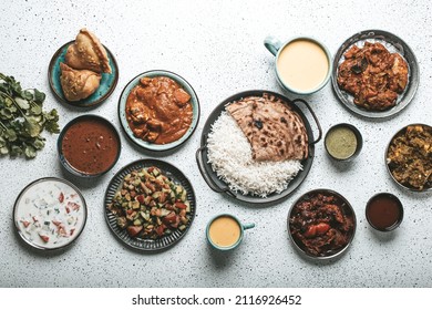 Indian Ethnic Food Buffet On White Concrete Table From Above: Curry, Samosa, Rice Biryani, Dal, Paneer, Chapatti, Naan, Chicken Tikka Masala, Mango Lassi, Dishes Of India For Dinner Background