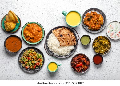 Indian Ethnic Food Buffet On White Concrete Table From Above: Curry, Samosa, Rice Biryani, Dal, Paneer, Chapatti, Naan, Chicken Tikka Masala, Mango Lassi, Dishes Of India For Dinner Background