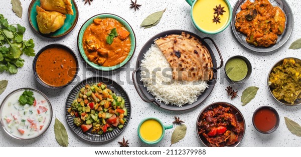 Indian ethnic food buffet on white concrete\
table from above: curry, samosa, rice biryani, dal, paneer,\
chapatti, naan, chicken tikka masala, mango lassi, dishes of India\
for dinner background