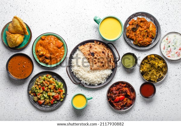 Indian ethnic food buffet on white concrete\
table from above: curry, samosa, rice biryani, dal, paneer,\
chapatti, naan, chicken tikka masala, mango lassi, dishes of India\
for dinner background