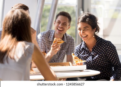 Indian excited woman laughing at funny joke, eating pizza with diverse colleagues in office, happy multi-ethnic employees having fun together during lunch, enjoying good conversation, emotions