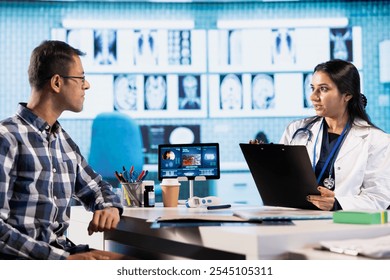 Indian expert explaining diagnostics through test results with a male patient at medical office, doing scan interpretation at check up with young man. Healthcare services on insurance.