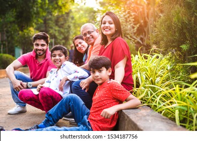 Indian Family Enjoying Picnic - Multi Generation Of Asian Family Sitting Over Or Near Small Wall In Park, Outdoor. Selective Focus