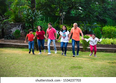 Indian Family Enjoying Picnic - Multi Generation Of Asian Family Walking Or Playing Chasing Game In Park Making Human Chain. Selective Focus