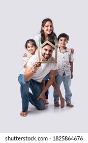 Indian Family Father, Mother, Son And Daughter Holding 3D Paper Model Of Home - Real Istate Concept In India