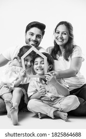 Indian Family Father, Mother, Son And Daughter Holding 3D Paper Model Of Home - Real Istate Concept In India