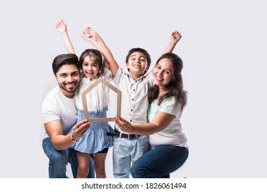 Indian Family Father, Mother, Son And Daughter Holding 3D Paper Model Of Home - Real Istate Concept In India