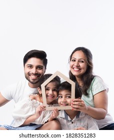 Indian Family Father, Mother, Son And Daughter Holding 3D Paper Model Of Home - Real Istate Concept In India