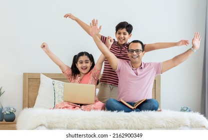 Indian family, father, son, daughter sitting on bed at cozy home, smiling with happiness, playing, using laptop, raising hands with success, win. Education, Technology, Creative Activity Concept - Shutterstock ID 2162900349