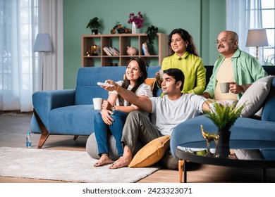 Indian family of four on sofa, engrossed in watching TV, switching channels with remote - Powered by Shutterstock