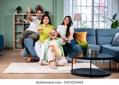 Indian family of four on sofa, engrossed in watching TV, switching channels with remote - Powered by Shutterstock