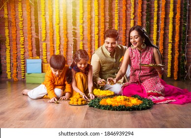 Indian Family Lighting Or Arranging Oil Lamp Or Diya Around Flower Rangoli On Diwali Festival Night