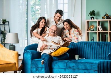 Indian family looking at Photo album while sitting on sofa, happy moment - Powered by Shutterstock