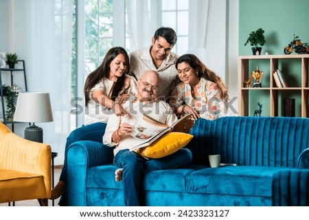 Indian family looking at Photo album while sitting on sofa, happy moment