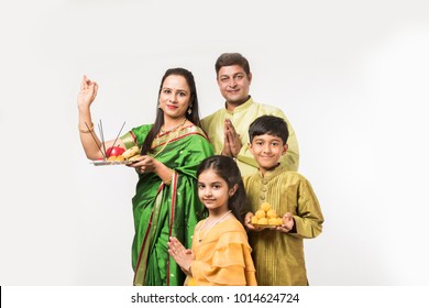Indian family performing Puja of something in traditional cloths with lady holding Pooja thali while standing isolated over white background