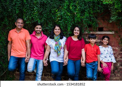 Indian Family Standing In Line Against Wall Covered With Creepers. Multi Generation Of Asian Family In Park Or Garden Having Fun, Healthy Family Life Concept