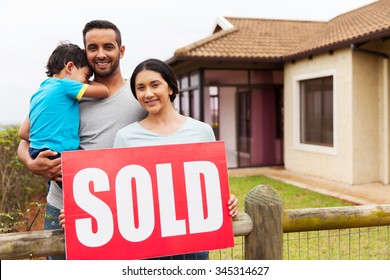 Indian Family Standing Outside Their House And Holding Sold Sign