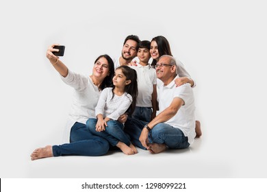 Indian Family Taking Selfie Picture With Smartphone While Sitting On White Background Includes 3 Generations. Selective Focus