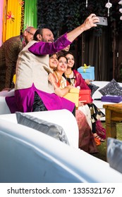 Indian Family Taking Selfie Picture Using Smartphone While Wearing Traditional Festival Cloths On Diwali/wedding Ceremony And Sitting On Sofa / Couch