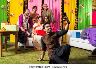 Indian Family Taking Selfie Picture Using Smartphone While Wearing Traditional Festival Cloths On Diwali/wedding Ceremony And Sitting On Sofa / Couch