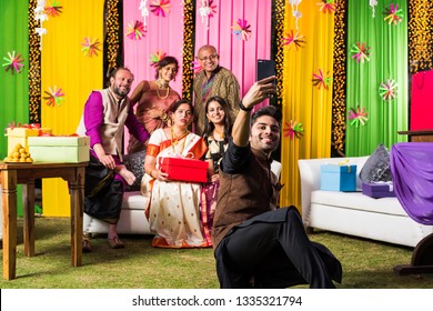 Indian Family Taking Selfie Picture Using Smartphone While Wearing Traditional Festival Cloths On Diwali/wedding Ceremony And Sitting On Sofa / Couch