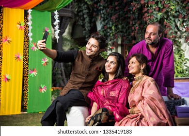 Indian Family Taking Selfie Picture Using Smartphone While Wearing Traditional Festival Cloths On Diwali/wedding Ceremony And Sitting On Sofa / Couch