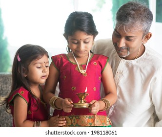 Indian family in traditional sari celebrate diwali or deepavali at home. Little girl hands holding oil lamp during festival of light.
