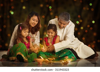Indian family in traditional sari lighting oil lamp and celebrating Diwali or deepavali, fesitval of lights at home. Little girl hands holding oil lamp indoors. - Shutterstock ID 311943323