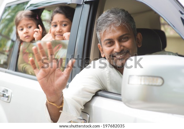 Indian family waving hands\
and saying goodbye, sitting in car ready to trip. Asian family\
lifestyle.