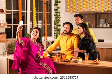 Indian family and young couple friends joyfully celebrating Diwali together in the modern home kitchen, sharing delicious food, laughter, stories around the table during this vibrant Hindu festival - Powered by Shutterstock