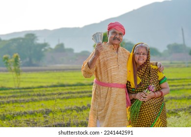 Indian farmer couple standing at agriculture field and showing rupees